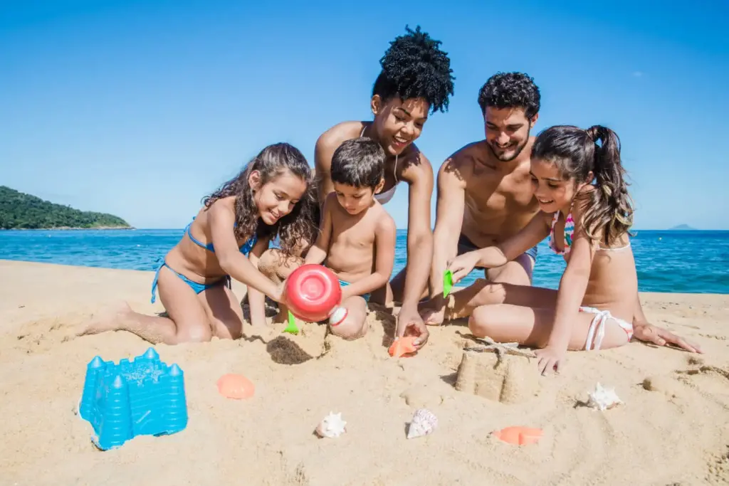 Família curtindo os feriados 2025 na praia, construindo castelos de areia com mar ao fundo.