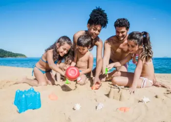 Família curtindo os feriados 2025 na praia, construindo castelos de areia com mar ao fundo.