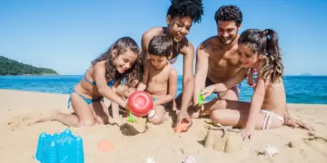 Família curtindo os feriados 2025 na praia, construindo castelos de areia com mar ao fundo.
