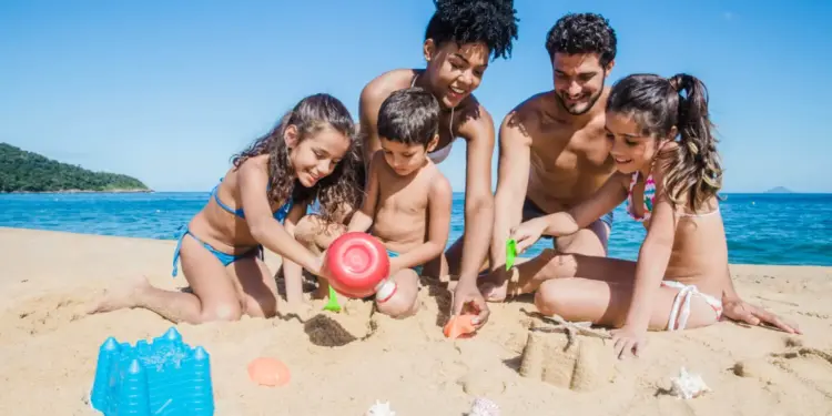 Família curtindo os feriados 2025 na praia, construindo castelos de areia com mar ao fundo.