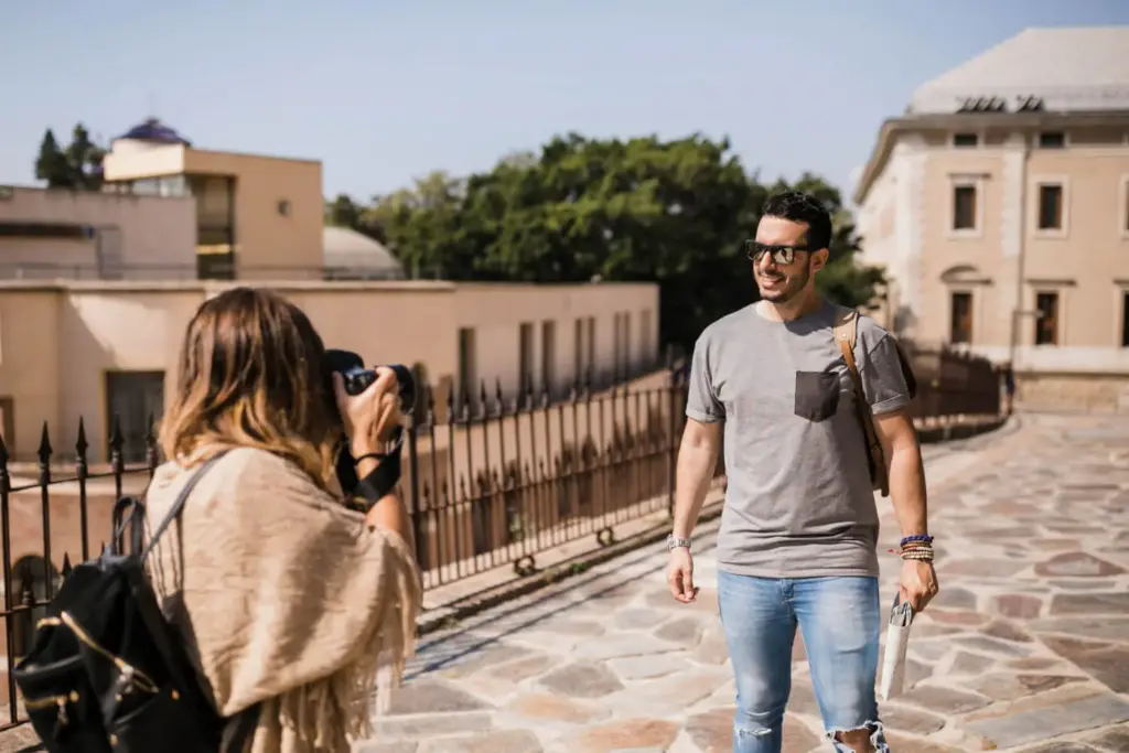 Homem posa para foto enquanto mulher o fotograga.