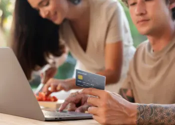 Open finance: homem comprando online com cartão de crédito e mulher ao fundo