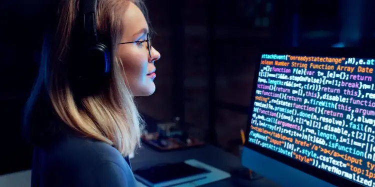Mulher jovem usando óculos em frente ao computador programando.