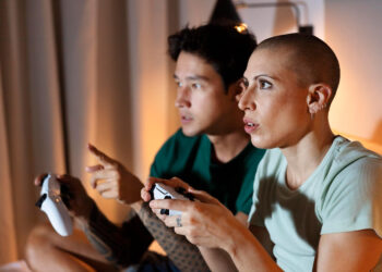 Duas pessoas jogando Avowed intensamente em ambiente aconchegante.