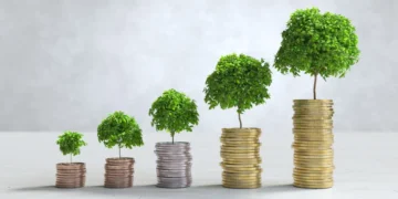 Como começar a investir? Guia passo a passo para iniciantes 3 Pilhas de moedas em sequência, uma ao lado da outra. Há pequenas árvores em cima de cada pilha, representando como começar a investir.