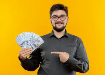 Homem aponta para cédulas, indicando ganho em dinheiro. Representando: economia compartilhada.