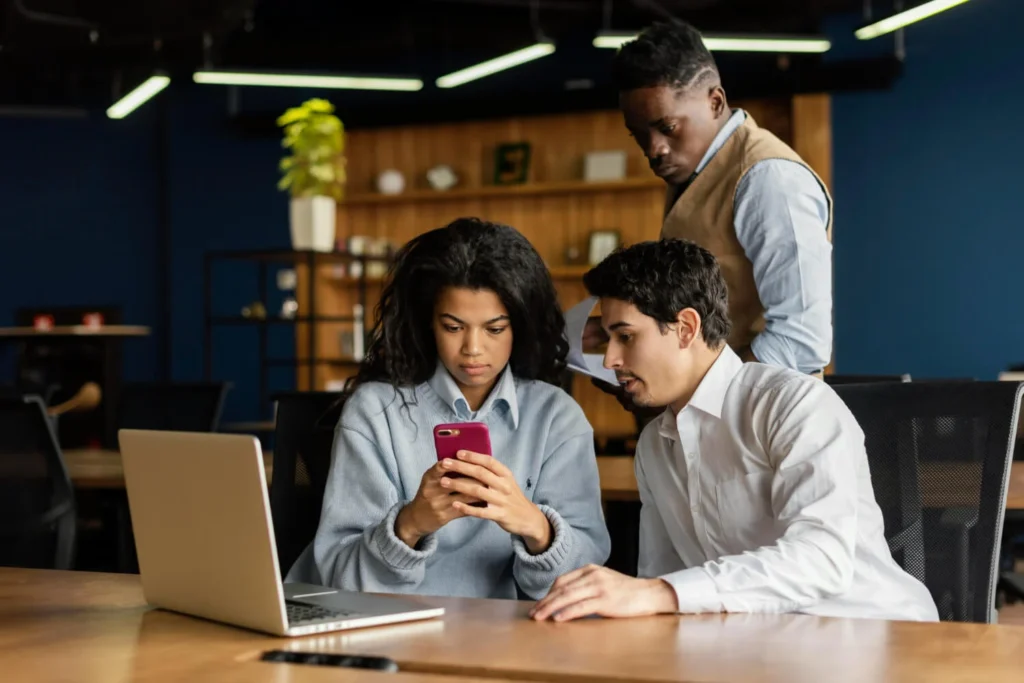 Pessoas em escritório analisam celular, discutindo franquias de tecnologia.