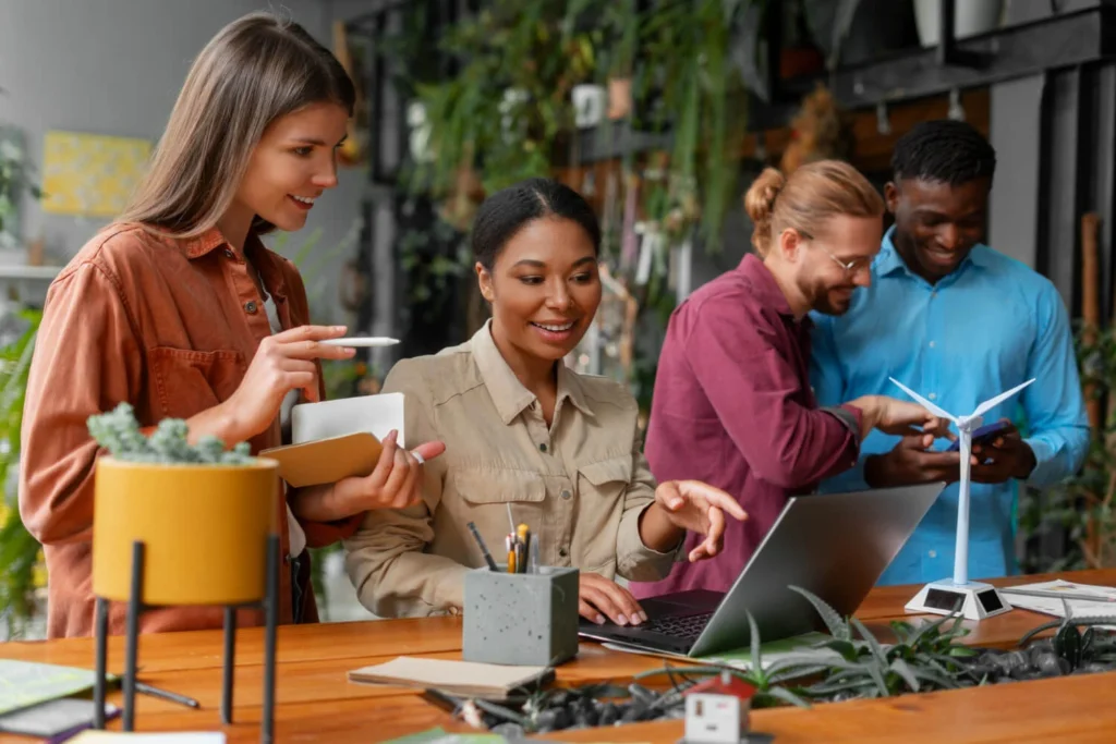 Grupo em ambiente sustentável pesquisa franquias de tecnologia em laptop e celular.