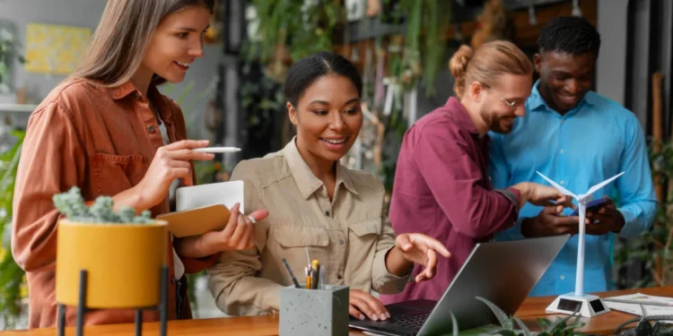 Grupo em ambiente sustentável pesquisa franquias de tecnologia em laptop e celular.