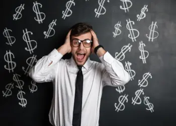 Homem com as mãos na cabeça à frente de uma quadro negro onde existem cifrões desenhados, representando golpes financeiros.