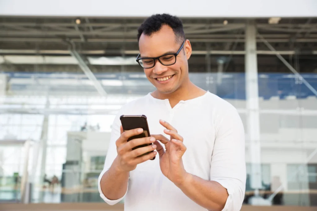 Homem sorridente usando um iPhone 16 em um ambiente moderno e iluminado.