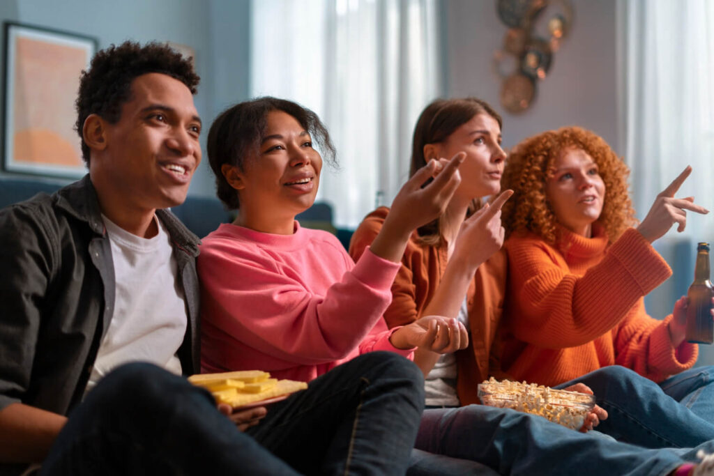 Grupo animado reage a séries novas para maratonar, segurando pipoca e bebidas no sofá.