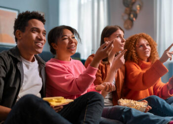 Grupo animado reage a séries novas para maratonar, segurando pipoca e bebidas no sofá.