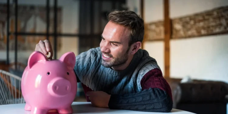 Homem sorridente poupando dinheiro em cofrinho, simbolizando investimentos para viver de renda.