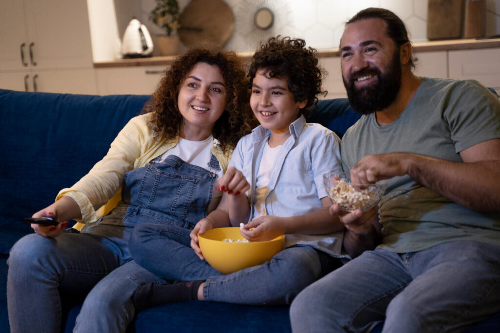 Família reunida no sofá assistindo a filmes e séries no Paramount+ e compartilhando pipoca.