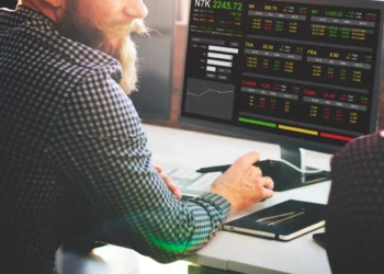 Homem tem a diante de si uma tela com gráficos que mostram variações de investimentos. Falando de ações e ETFs.