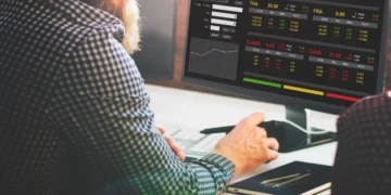 Homem tem a diante de si uma tela com gráficos que mostram variações de investimentos. Falando de ações e ETFs.