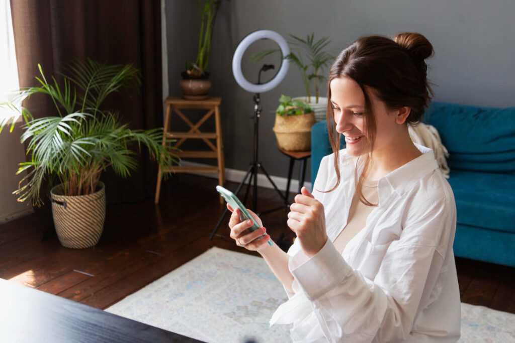 Mulher animada usando smartphone em ambiente com plantas analisando empolgada aplicativos para lucrar.