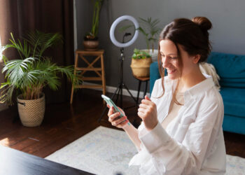 Mulher animada usando smartphone em ambiente com plantas analisando empolgada aplicativos para lucrar.