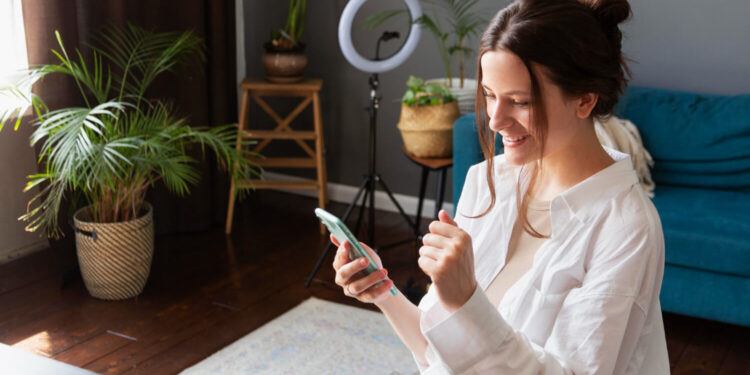 Mulher animada usando smartphone em ambiente com plantas analisando empolgada aplicativos para lucrar.