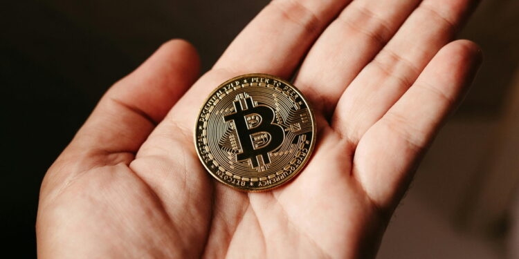 Bitcoin recua para menos de US$ 79 mil em meio a tensões tarifárias e expectativas de juros nos EUA 14 Pessoa segura moeda física de Bitcoin na palma das mãos.