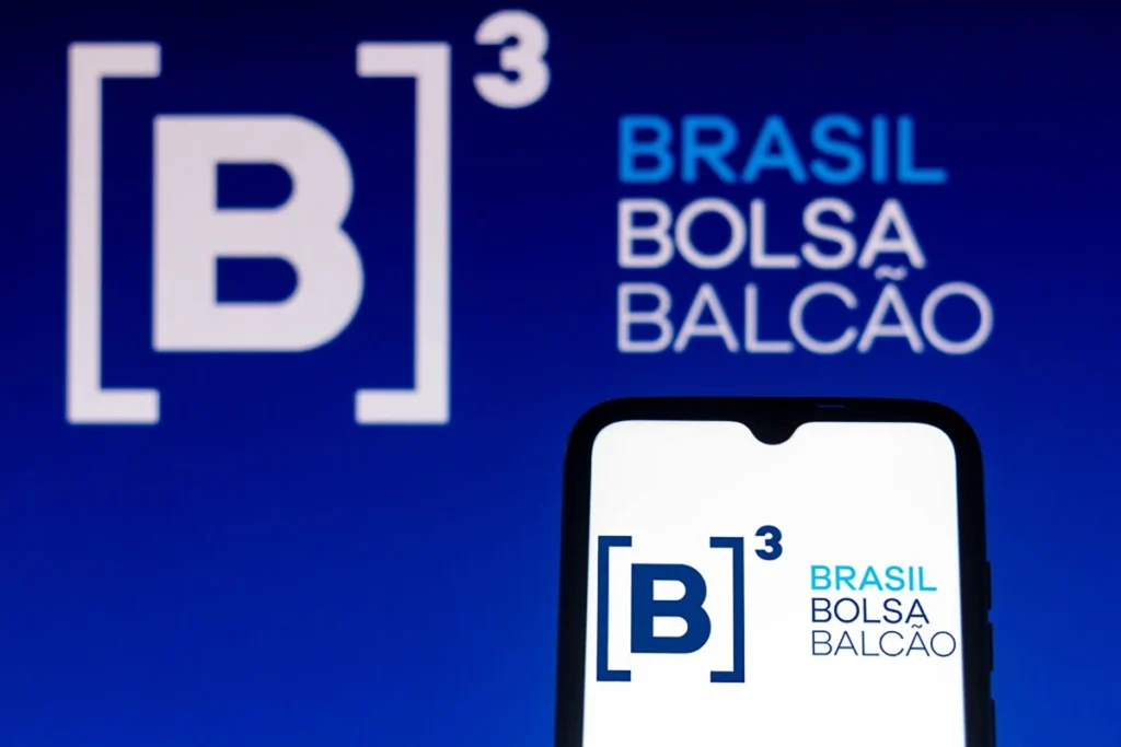 Logomarca da B3 em perspectiva de banner ao fundo e na tela de um celular em primeiro plano.