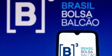 Logomarca da B3 em perspectiva de banner ao fundo e na tela de um celular em primeiro plano.