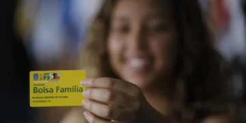 Bolsa Família 2025: novas regras e como se inscrever 1 Mulher sorridente segura e evidencia o seu cartão do Bolsa Família.