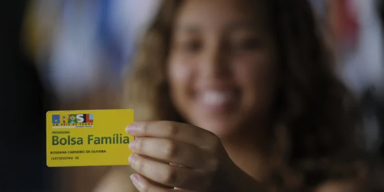 Bolsa Família 2025: novas regras e como se inscrever 14 Mulher sorridente segura e evidencia o seu cartão do Bolsa Família.