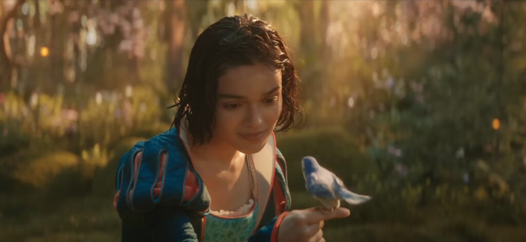 Branca de Neve 2025: O que funcionou e o que falhou na releitura da Disney? 26 Branca de Neve em "Branca de Neve 2025", sorrindo em um bosque enquanto segura um passarinho azul.