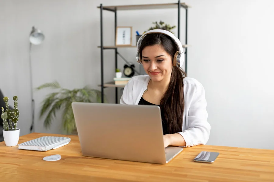 Mulher sorri ao aproveitar vagas de emprego online. Ela está com fones de ouvido e usando um notebook.