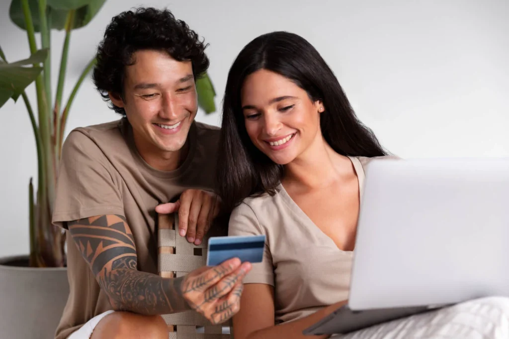 Casal sorridente usando um laptop e segurando um cartão, simbolizando cartões de crédito sem anuidade.