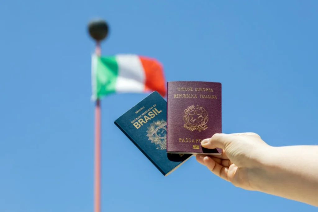 Pessoa segura um passaporte brasileiro e um italiano. Ao fundo, a bandeira da Itália tremula. Falando sobre cidadania italiana.