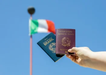 Pessoa segura um passaporte brasileiro e um italiano. Ao fundo, a bandeira da Itália tremula. Falando sobre cidadania italiana.