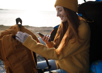 Jovem organizando sua mochila e verificando o celular, pensando sobre como planejar um intercâmbio.