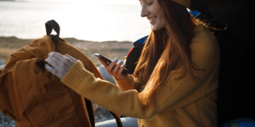 Guia Completo para Estudar Fora: Como Planejar um Intercâmbio de Sucesso? 7 Jovem organizando sua mochila e verificando o celular, pensando sobre como planejar um intercâmbio.