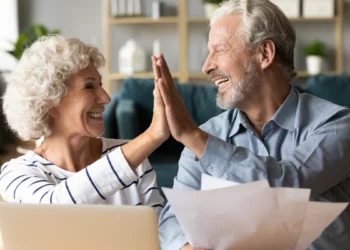Casal de idosos sorridentes unem as mãos em um cumprimento. Falando sobre décimo terceiro salário de aposentados e pensionistas.