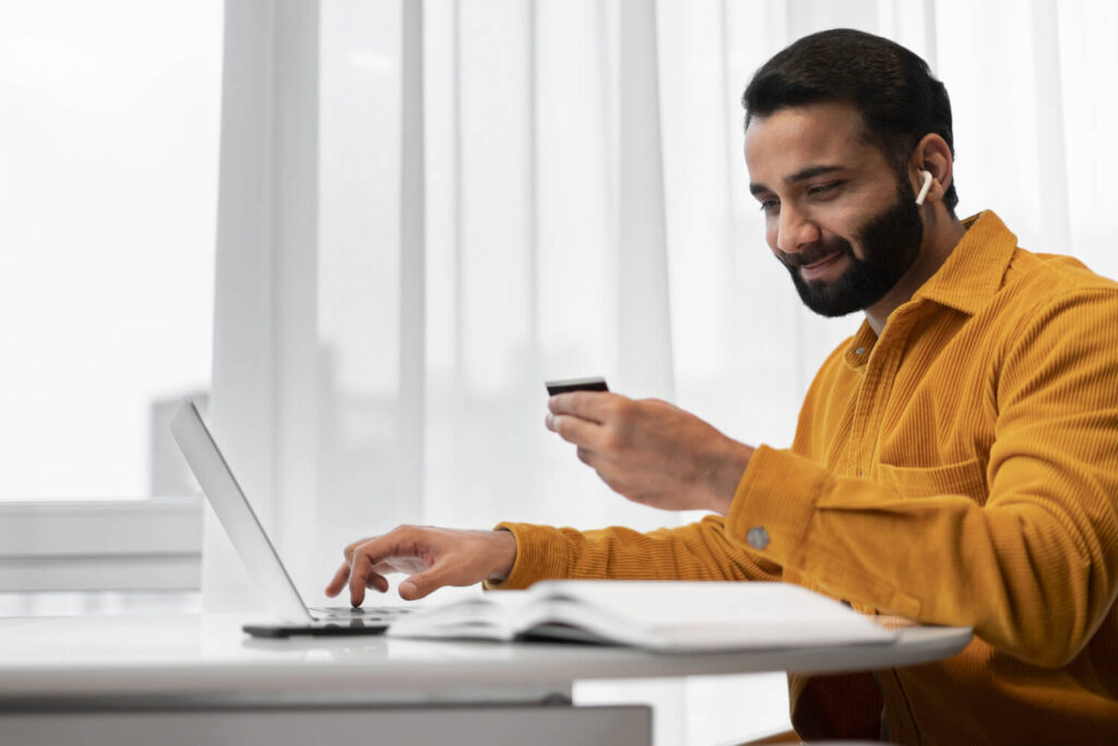 Homem sorrindo ao usar cartão e laptop, mostrando que milhas valem dinheiro e geram benefícios.