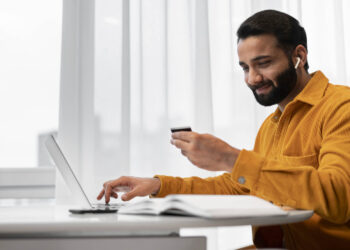 Homem sorrindo ao usar cartão e laptop, mostrando que milhas valem dinheiro e geram benefícios.