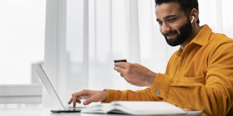 Homem sorrindo ao usar cartão e laptop, mostrando que milhas valem dinheiro e geram benefícios.