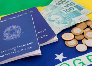 Duas carteiras de trabalho sobre uma bandeira do Brasil com algumas moedas e notas de R$ 100 ao lado. Falando de empréstimo consignado CLT.