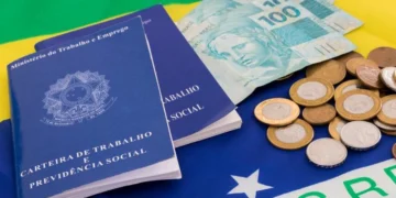 Duas carteiras de trabalho sobre uma bandeira do Brasil com algumas moedas e notas de R$ 100 ao lado. Falando de empréstimo consignado CLT.