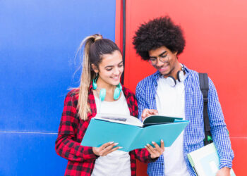 Dois jovens estudantes sorrindo enquanto estudam juntos, simbolizando a prática para falar inglês fluente.