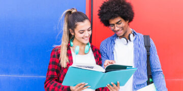 Dois jovens estudantes sorrindo enquanto estudam juntos, simbolizando a prática para falar inglês fluente.