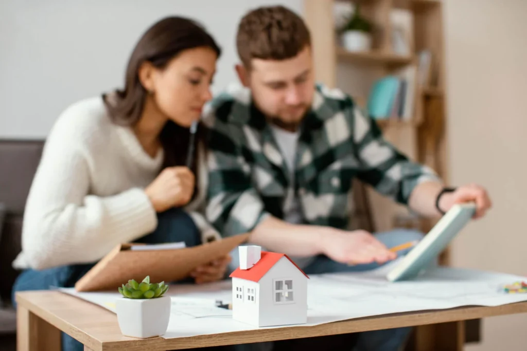 Casal analisa documentos para financiamento imobiliário em 2025, com casa em miniatura à frente.