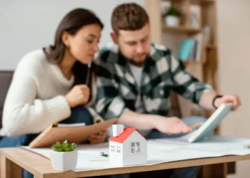Casal analisa documentos para financiamento imobiliário em 2025, com casa em miniatura à frente.