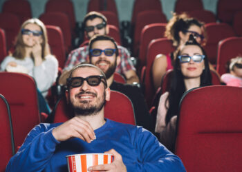 Pessoas assistindo a um dos filmes mais esperados no cinema, usando óculos 3D e comendo pipoca.