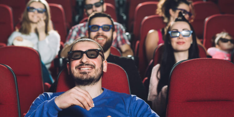 Pessoas assistindo a um dos filmes mais esperados no cinema, usando óculos 3D e comendo pipoca.