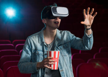 Homem com óculos VR e pipoca em cinema interagindo com filmes sci-fi de forma imersiva.