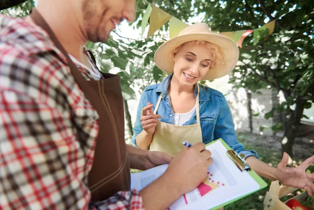 Agricultores analisam documentos e discutem gestão rural em feira ao ar livre, cercados por árvores.